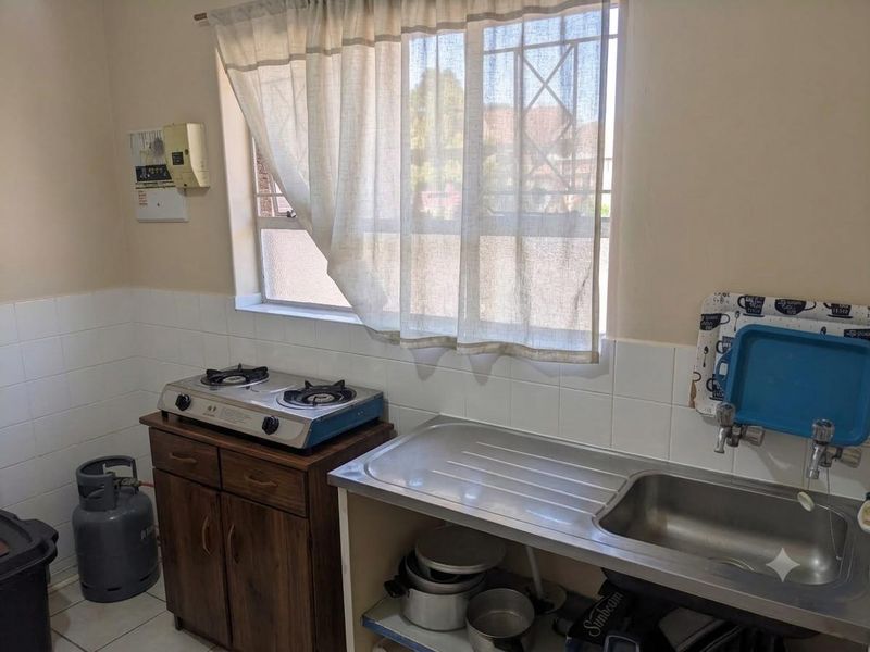 A functional kitchen area featuring a stainless steel sink, tiled splashback, and gas hob with wooden cabinetry.