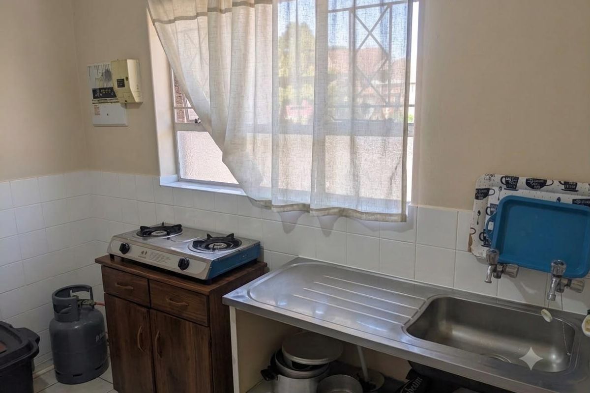 A functional kitchen area featuring a stainless steel sink, tiled splashback, and gas hob with wooden cabinetry.
