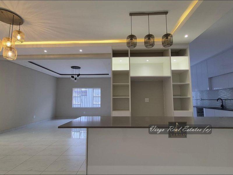 Spacious open-plan living and kitchen area featuring modern built-in cabinetry, a central island, recessed lighting, and sleek tiled flooring throughout.