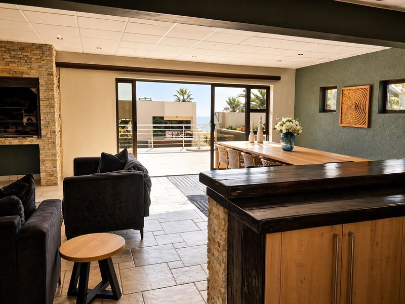 Spacious open-plan living and dining area featuring a stone-clad fireplace, tiled flooring, and large sliding doors opening to an outdoor balcony with coastal views.
