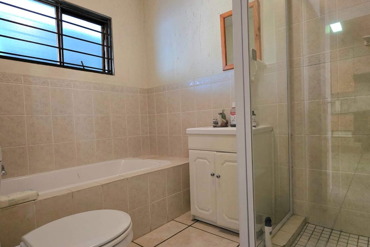 A functional bathroom featuring a built-in bathtub, separate shower enclosure, and vanity cabinet with neutral ceramic tiling throughout.