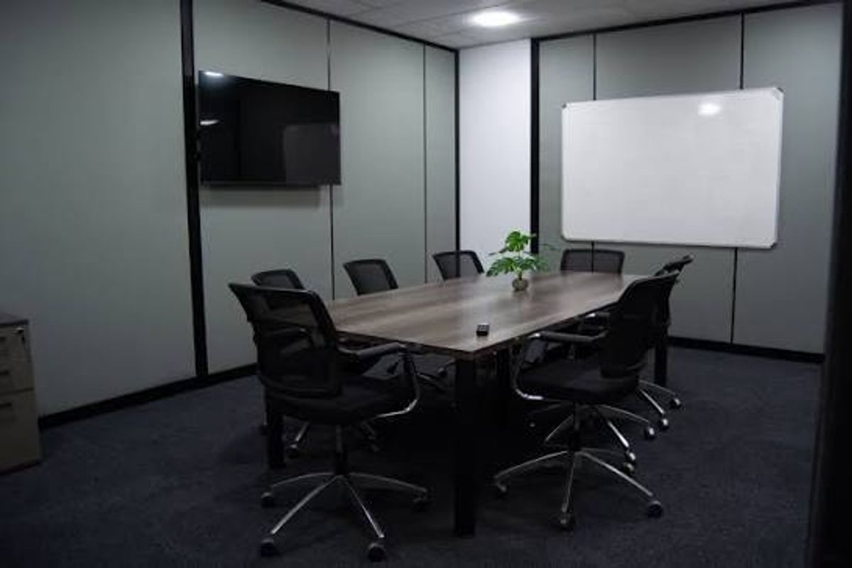 A professional office meeting room featuring partitioned walls, a wall-mounted whiteboard, a television, and recessed ceiling lighting.