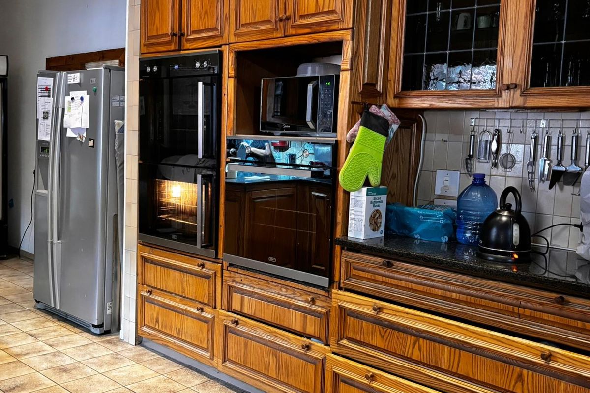 A traditional kitchen featuring extensive wooden cabinetry, built-in double ovens, a microwave niche, and granite countertops with a tiled backsplash.