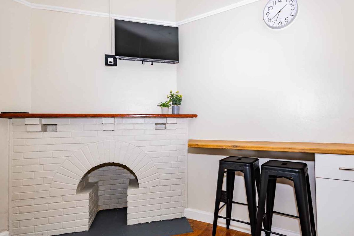 A living area featuring a painted brick fireplace, timber mantle, and a built-in breakfast bar with wooden countertop.