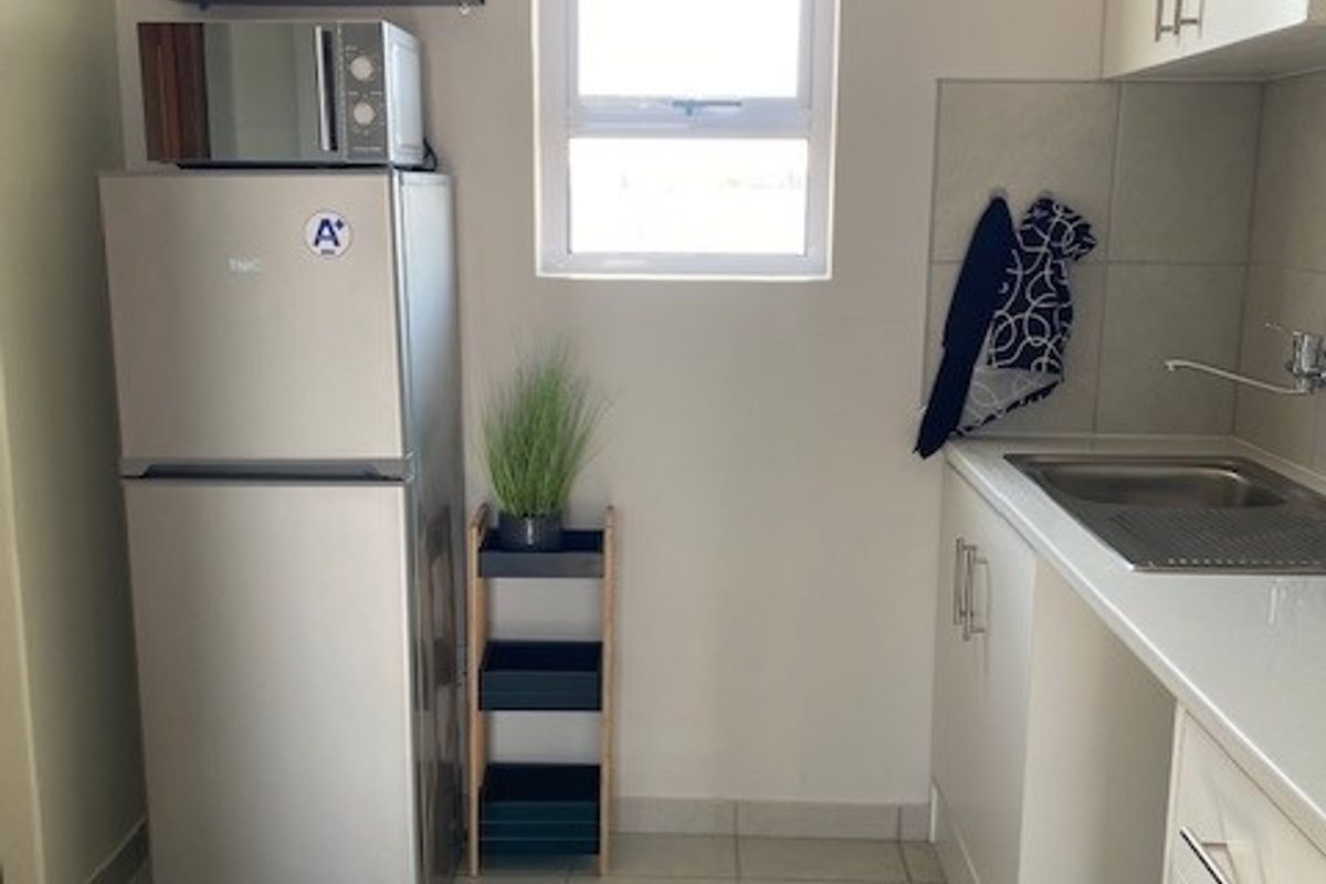 A compact kitchen featuring white cabinetry, tiled flooring, and a stainless steel sink, providing a functional and clean workspace.