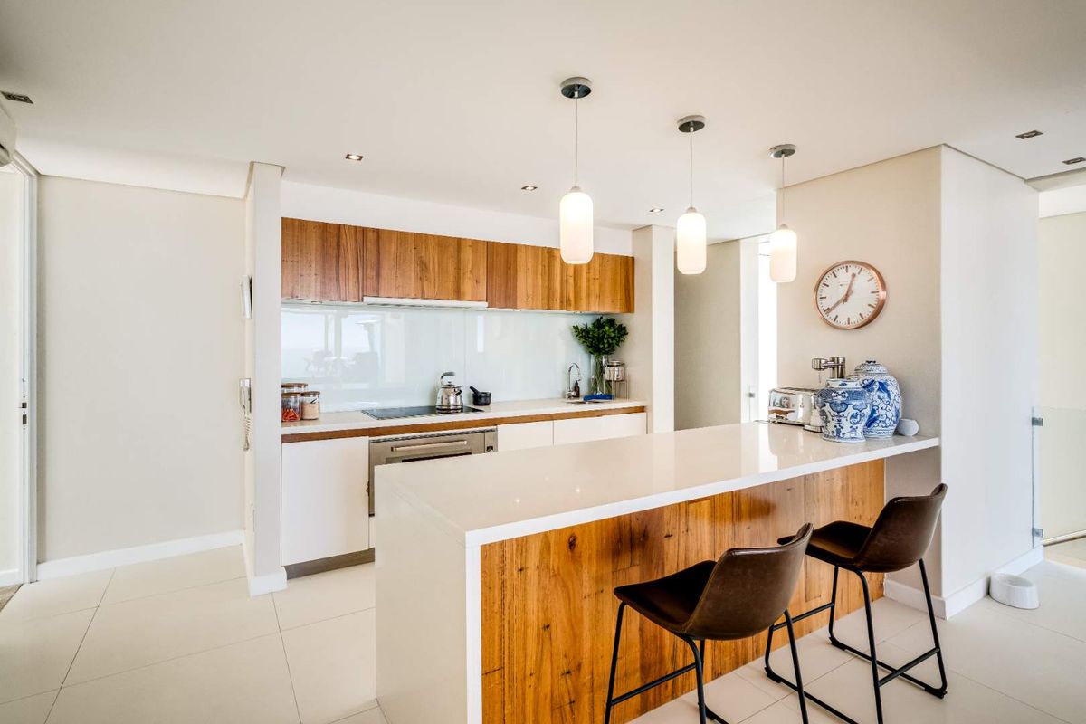 Modern kitchen featuring wood-grain cabinetry, white stone countertops, a breakfast bar, and integrated appliances, creating a clean and functional culinary space.