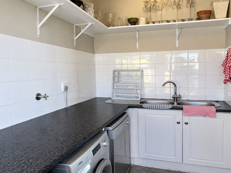 Functional laundry area featuring a double stainless steel sink, laminate countertops, white tiled backsplash, and convenient under-counter cabinetry with plumbing for appliances.