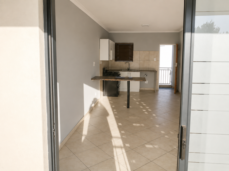 A functional, empty kitchen featuring tiled flooring, built-in cabinetry, a stove, and a breakfast counter, with direct access to an outdoor balcony.