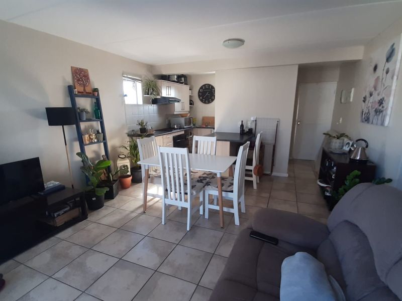 Open-plan living and dining area featuring tiled flooring and a compact kitchen with built-in cabinetry and an integrated breakfast bar.