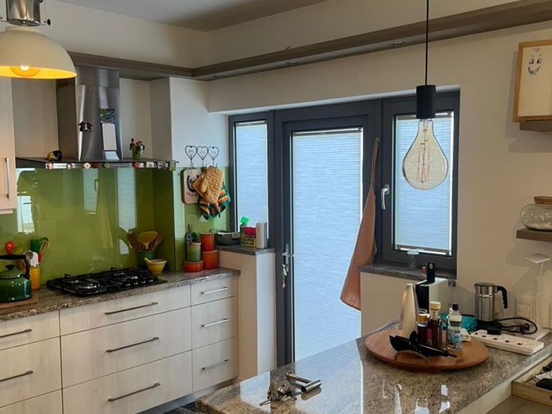 Modern kitchen featuring granite countertops, a vibrant glass splashback, gas hob, stainless steel extractor, and direct access to the exterior via a glass-paneled door.