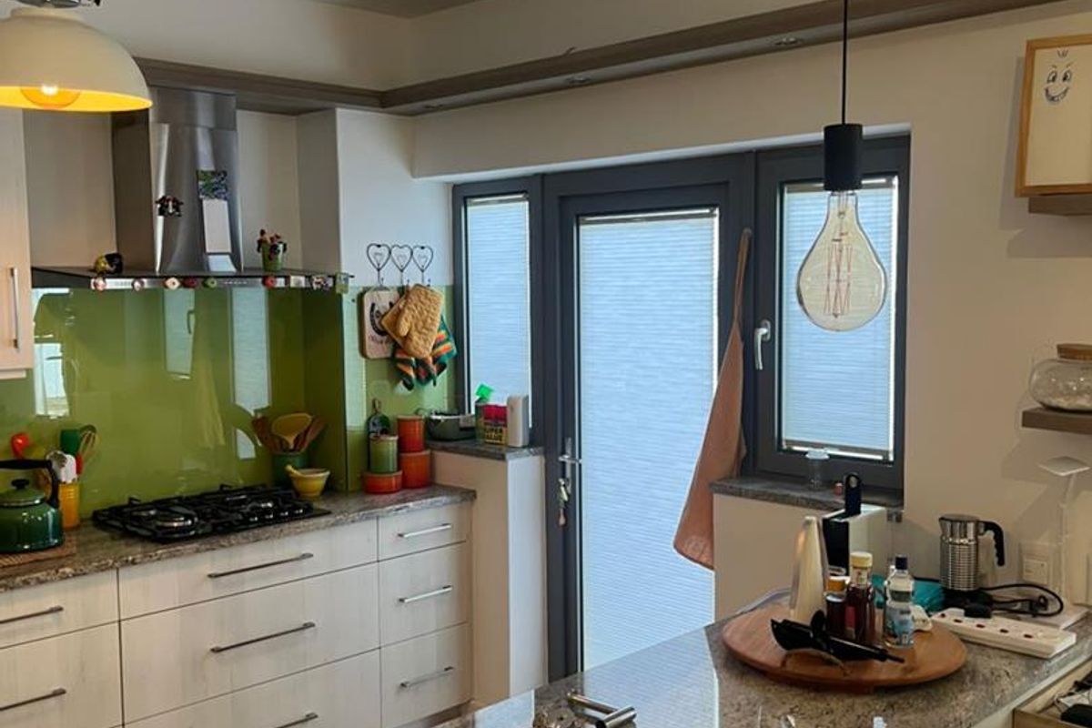 Modern kitchen featuring granite countertops, a vibrant glass splashback, gas hob, stainless steel extractor, and direct access to the exterior via a glass-paneled door.