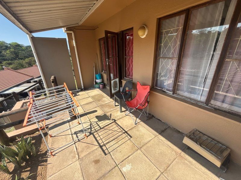 A covered outdoor patio area featuring tiled flooring, security-fitted windows, and an external wall light, offering a functional space for outdoor relaxation.