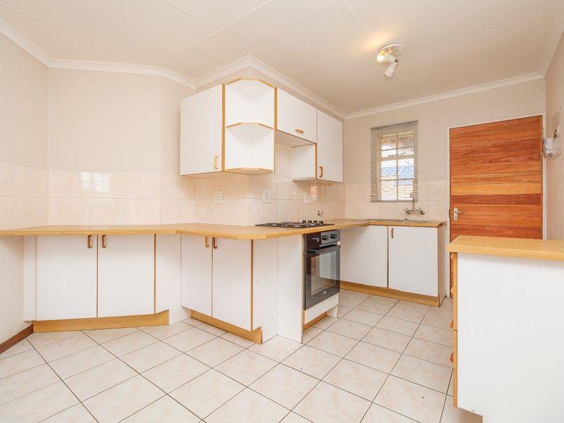 A functional, empty kitchen featuring white cabinetry, laminate countertops, a built-in oven with gas hob, and tiled flooring.