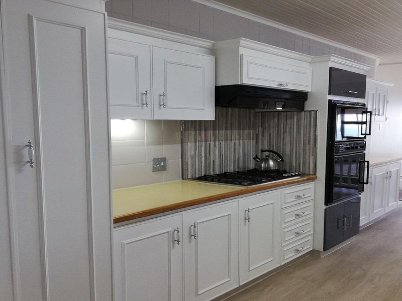A well-maintained kitchen featuring white cabinetry, a gas hob with extractor fan, built-in oven, and a tiled backsplash.