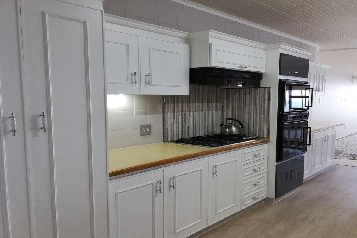 A well-maintained kitchen featuring white cabinetry, a gas hob with extractor fan, built-in oven, and a tiled backsplash.