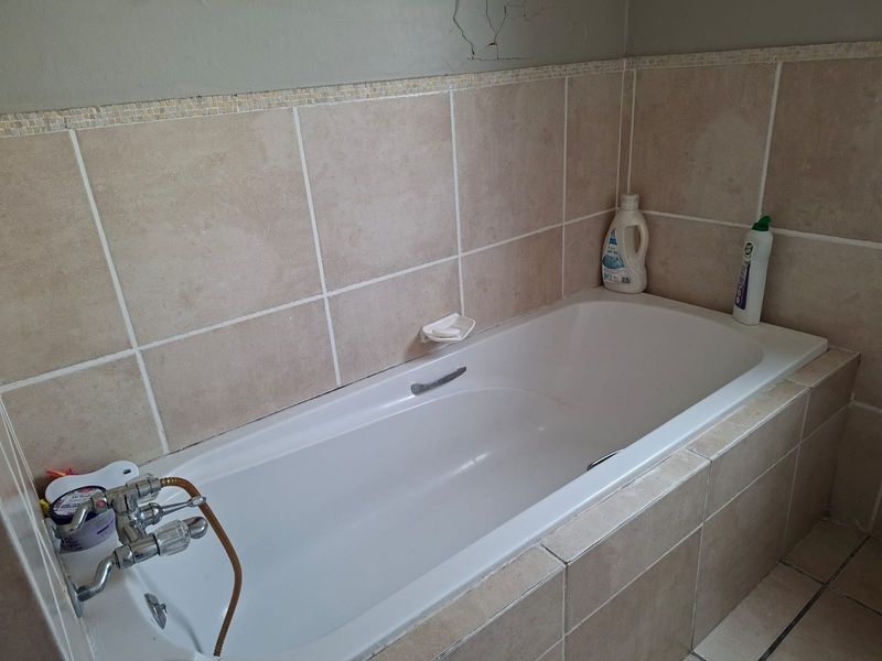 A bathroom featuring a built-in bathtub with chrome mixer tap and neutral ceramic wall tiling, showing visible plaster cracking on the upper wall.