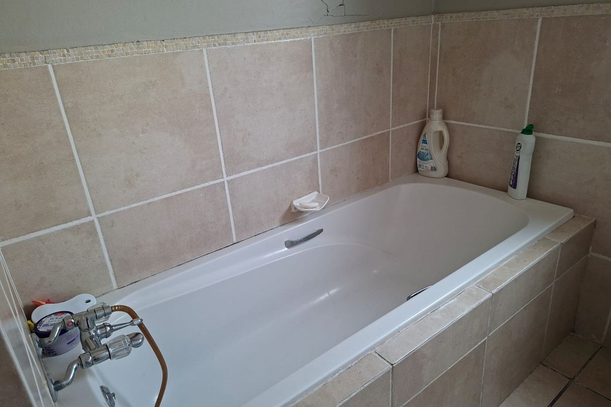 A bathroom featuring a built-in bathtub with chrome mixer tap and neutral ceramic wall tiling, showing visible plaster cracking on the upper wall.