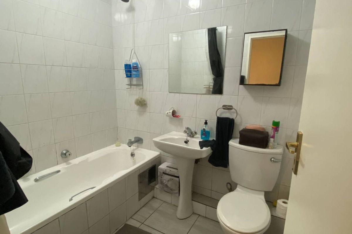A functional bathroom featuring a white bathtub with shower head, pedestal basin, and standard toilet with full-height wall tiling.