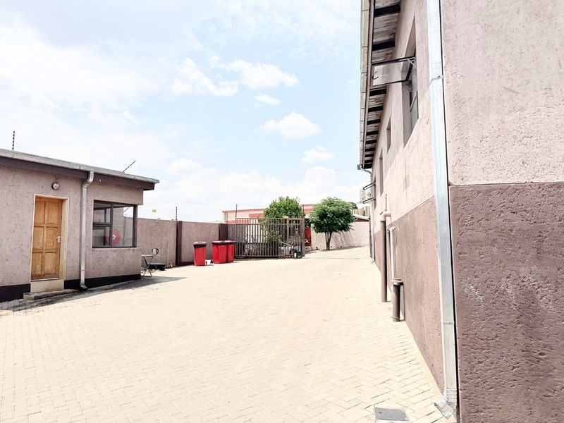A paved rear courtyard area featuring perimeter walls with electric fencing, a metal security gate, and exterior building access points.