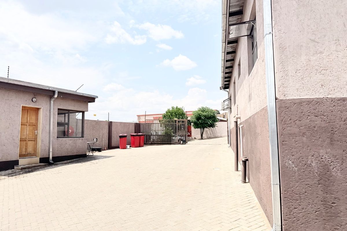 A paved rear courtyard area featuring perimeter walls with electric fencing, a metal security gate, and exterior building access points.