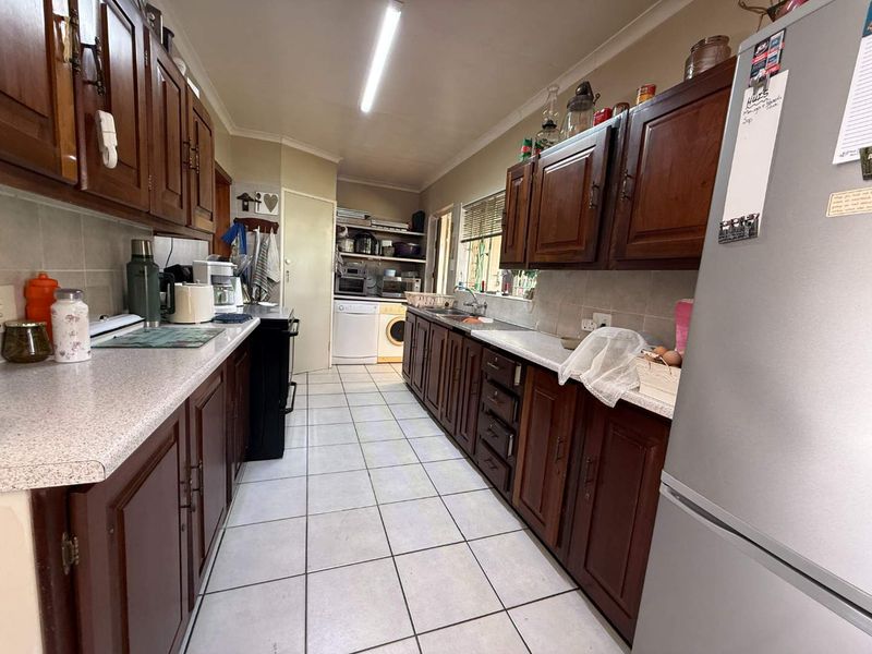 A functional galley-style kitchen featuring traditional wooden cabinetry, laminate countertops, tiled flooring, and integrated space for laundry appliances.