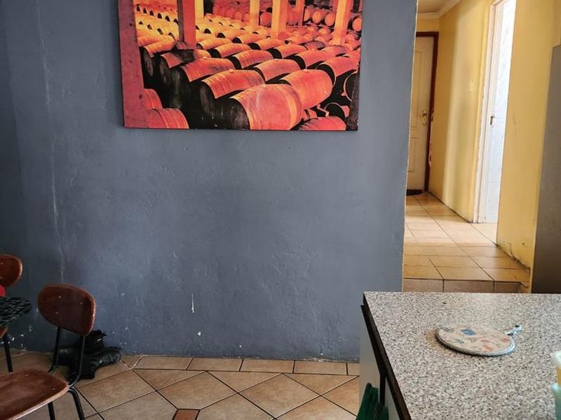 A kitchen area featuring tiled flooring and a laminate countertop, showing signs of wear including ceiling water damage and scuffed wall finishes.