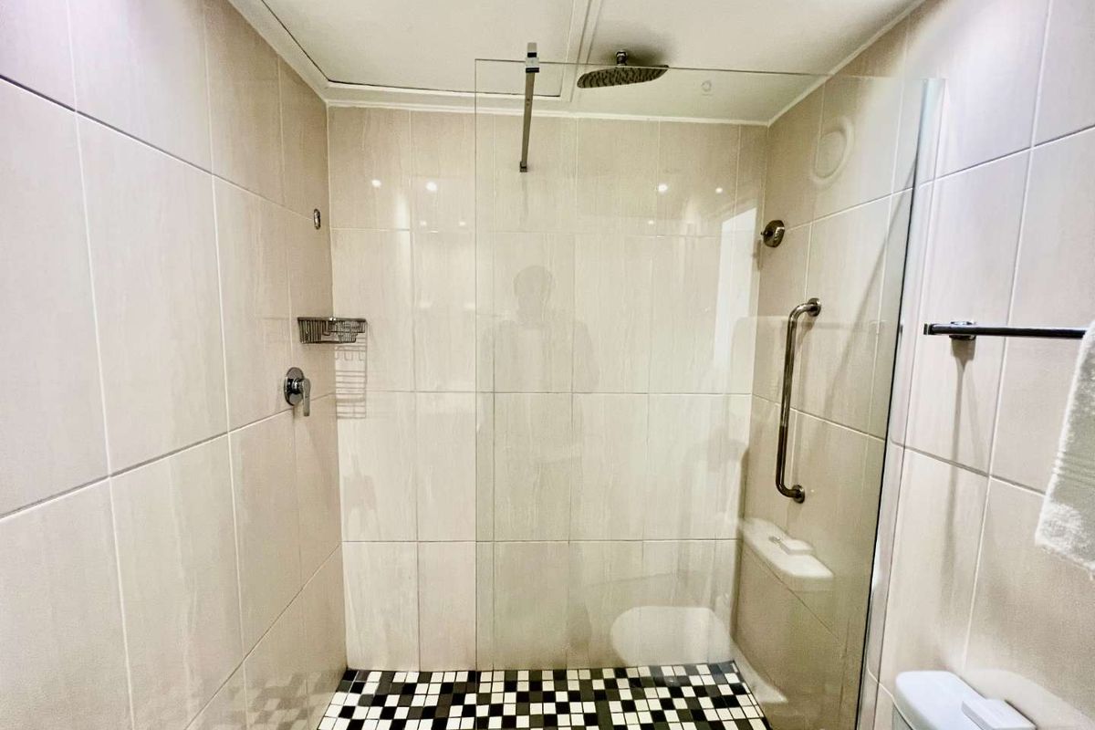 A modern walk-in shower featuring neutral wall tiling, a glass partition, a rainfall showerhead, and a distinctive black and white mosaic tiled floor.