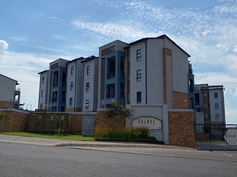 Exterior view of the Grange apartment complex featuring a brick boundary wall, secure gated entrance, and modern multi-story residential building facade.
