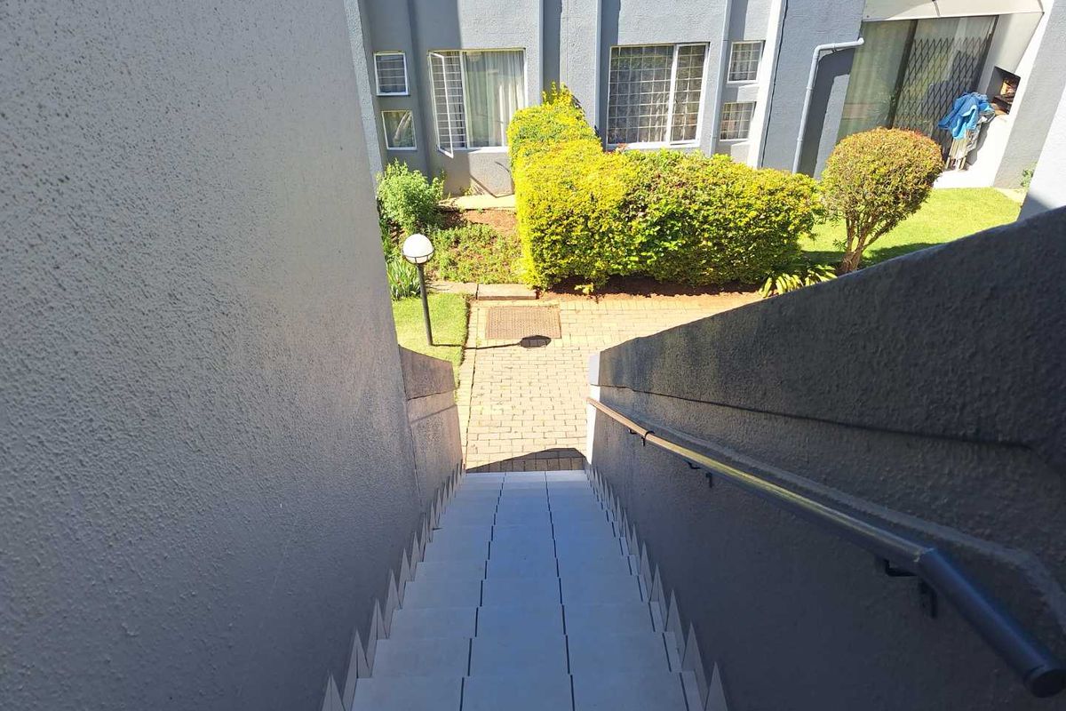 An exterior view looking down a tiled staircase towards a paved walkway and landscaped garden area within the townhouse complex.