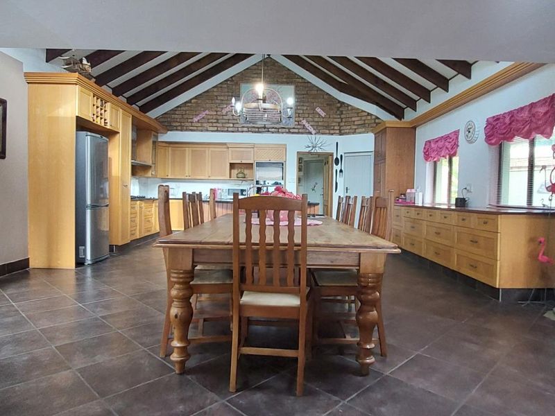 Spacious open-plan kitchen and dining area featuring exposed timber ceiling beams, a brick feature wall, and extensive built-in wooden cabinetry.