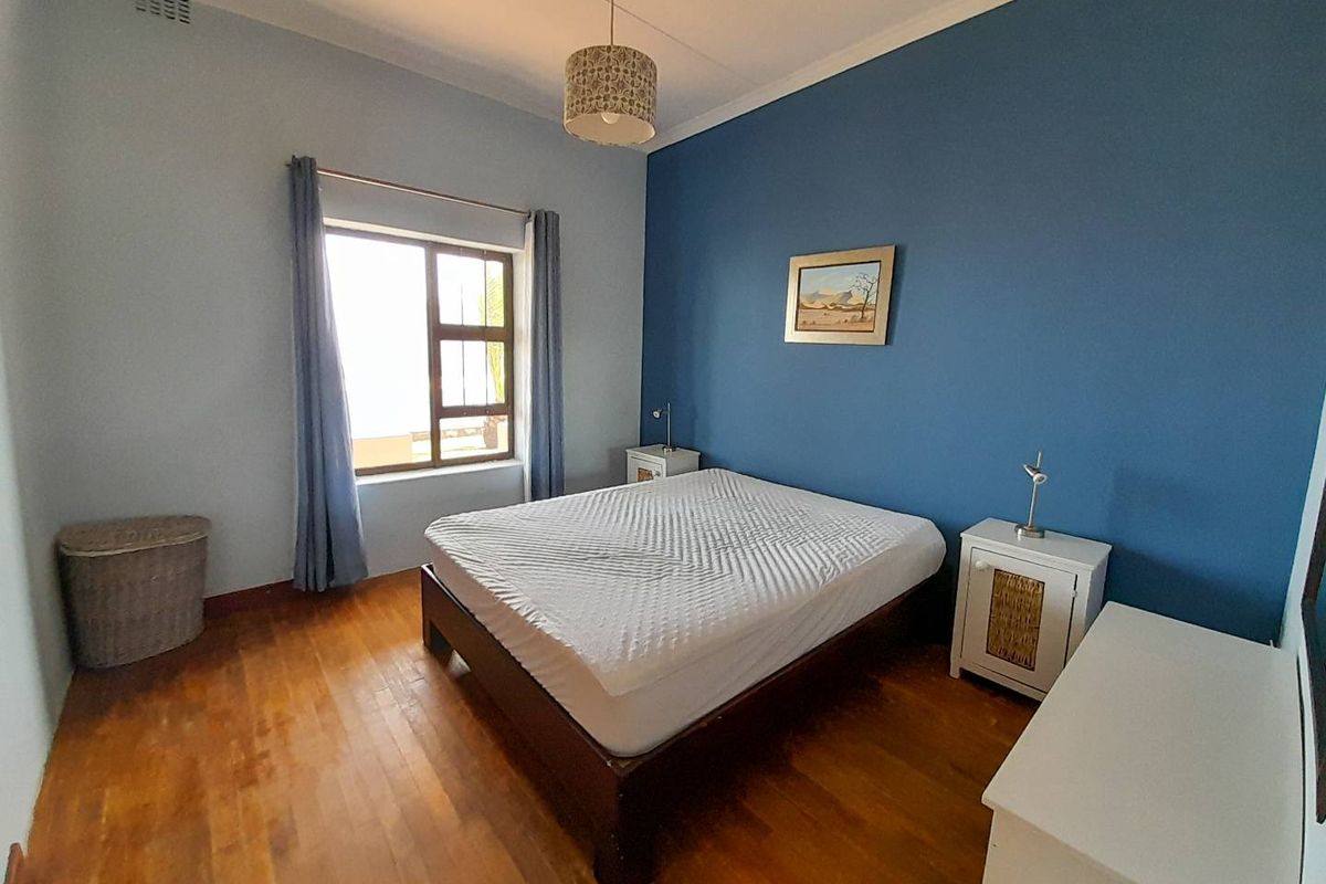 A bedroom featuring polished timber flooring, a blue accent wall, and a window providing natural light.
