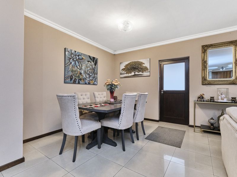 A well-maintained dining area featuring neutral tiled flooring, cove cornicing, and a classic timber door with a glass insert.