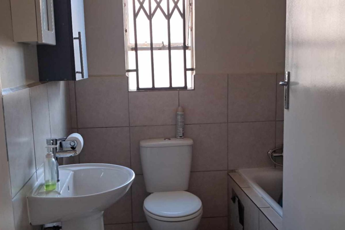A functional bathroom featuring a pedestal basin, standard toilet, and a bathtub with tiled walls and security bars on the window.