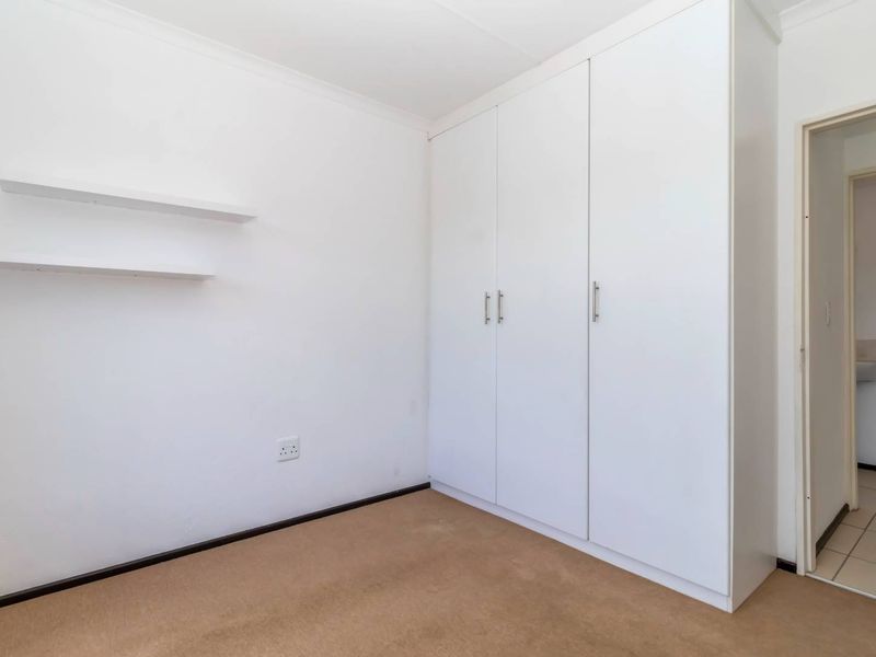 A clean, empty bedroom featuring neutral carpeted flooring, white built-in cupboards, and wall-mounted floating shelves.