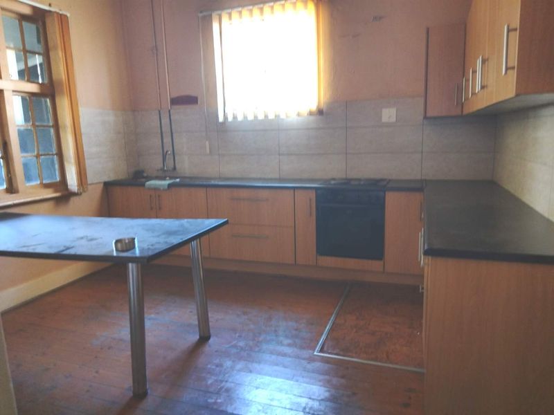 A dated kitchen featuring built-in cabinetry, laminate countertops, and an integrated oven and hob, set against a tiled backsplash and timber flooring.