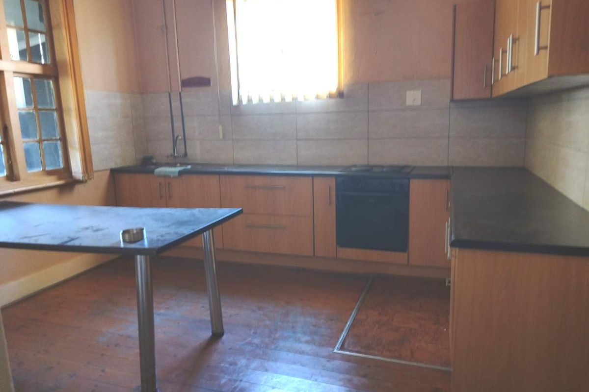 A dated kitchen featuring built-in cabinetry, laminate countertops, and an integrated oven and hob, set against a tiled backsplash and timber flooring.