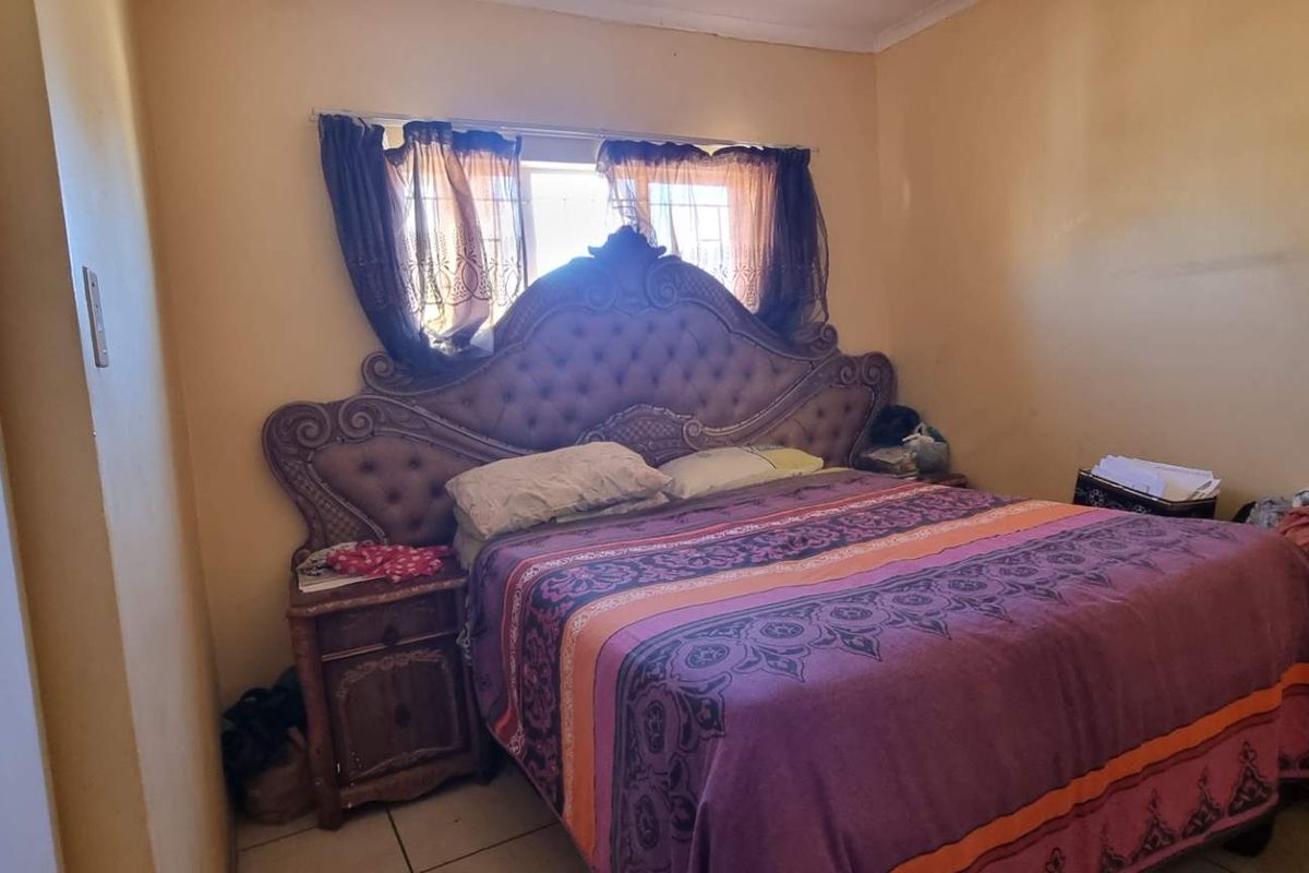 A bedroom featuring tiled flooring, a built-in wardrobe, and a window with security bars. The room requires cosmetic updates to the wall finishes.