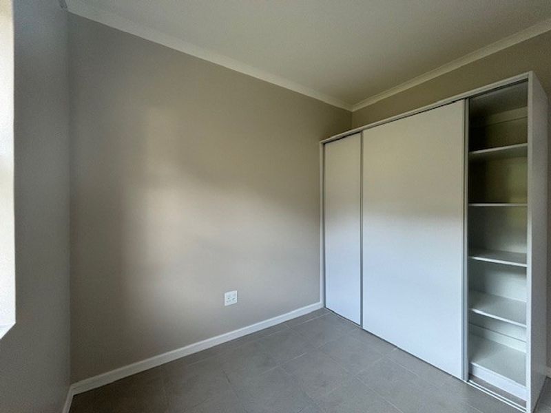 A clean, empty bedroom featuring neutral wall tones, tiled flooring, and a functional built-in wardrobe with shelving.