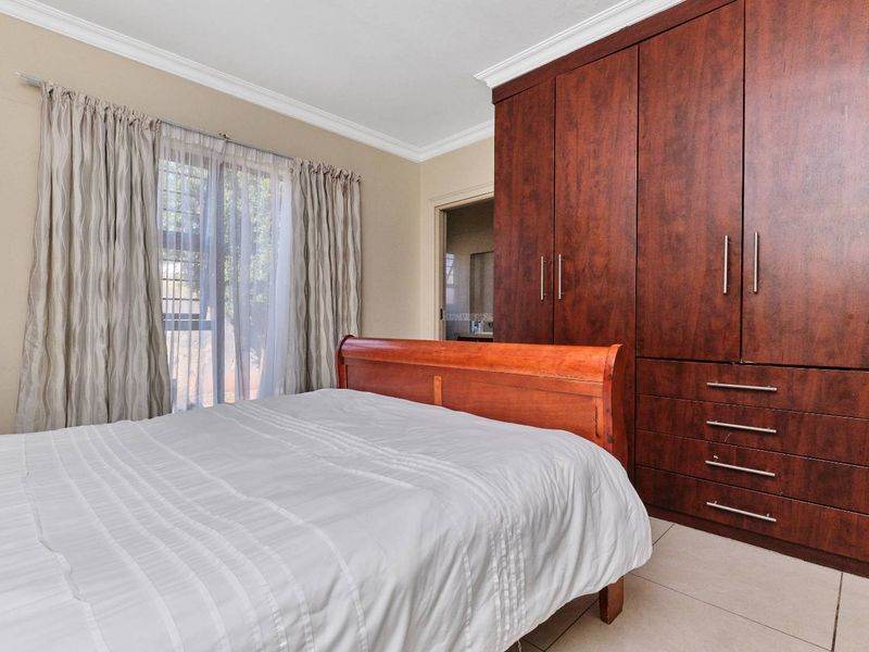 A well-maintained bedroom featuring dark wood built-in cupboards, tiled flooring, and crown molding, with direct access to an en-suite bathroom.