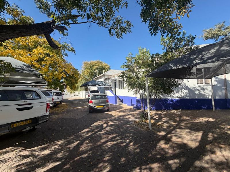 Front exterior view of the property featuring a paved driveway, shade cloth carports, and access steps leading to the building entrance.