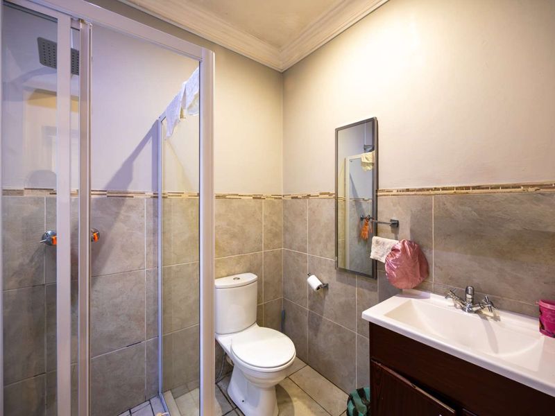 A functional bathroom featuring a shower enclosure, toilet, and a vanity basin with tiled walls and flooring.