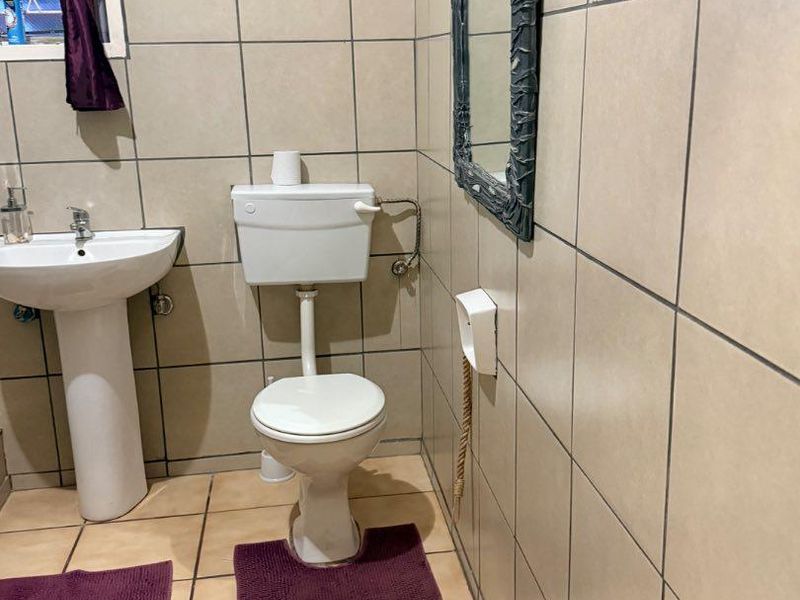 A functional bathroom featuring a pedestal basin, ceramic toilet, and full-height wall tiling.