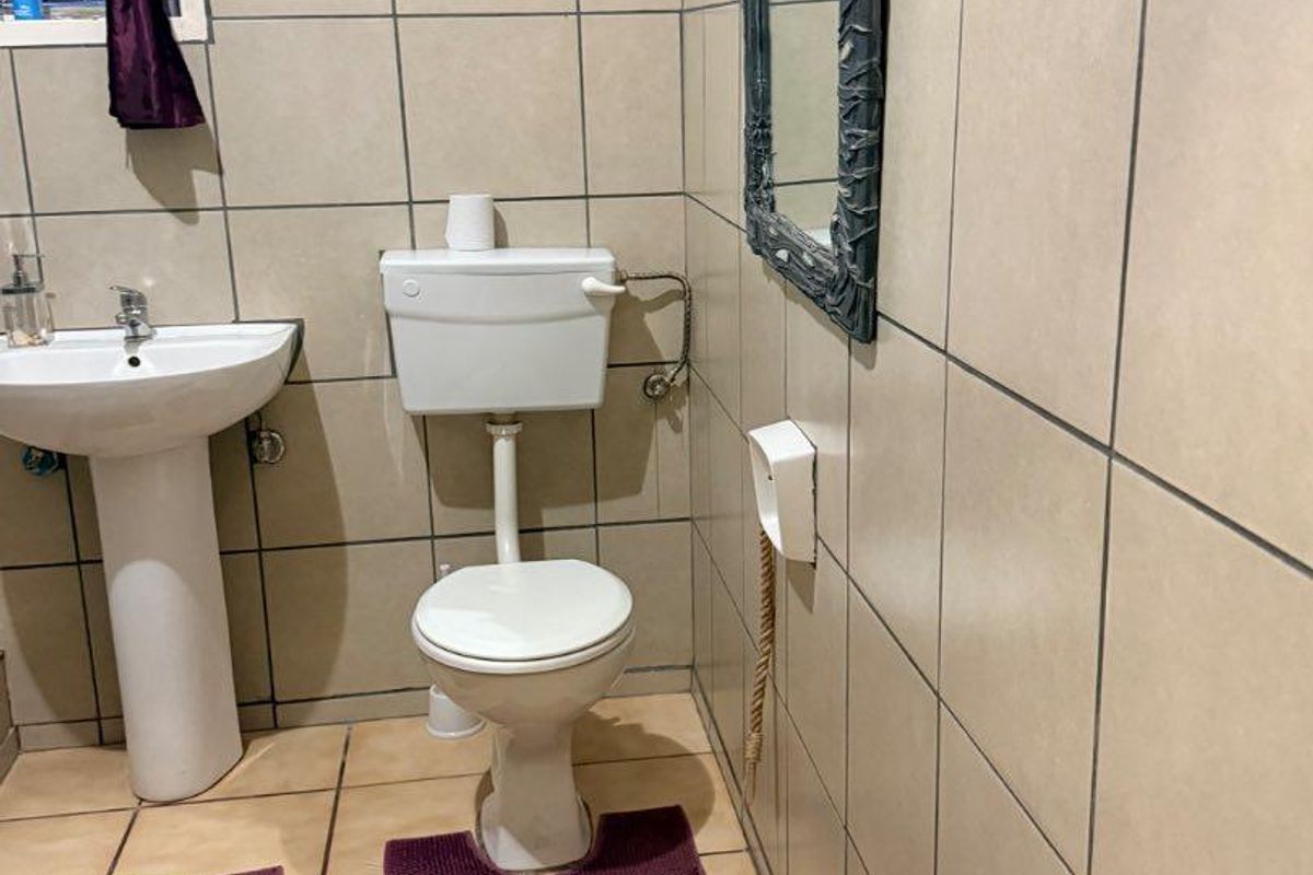 A functional bathroom featuring a pedestal basin, ceramic toilet, and full-height wall tiling.