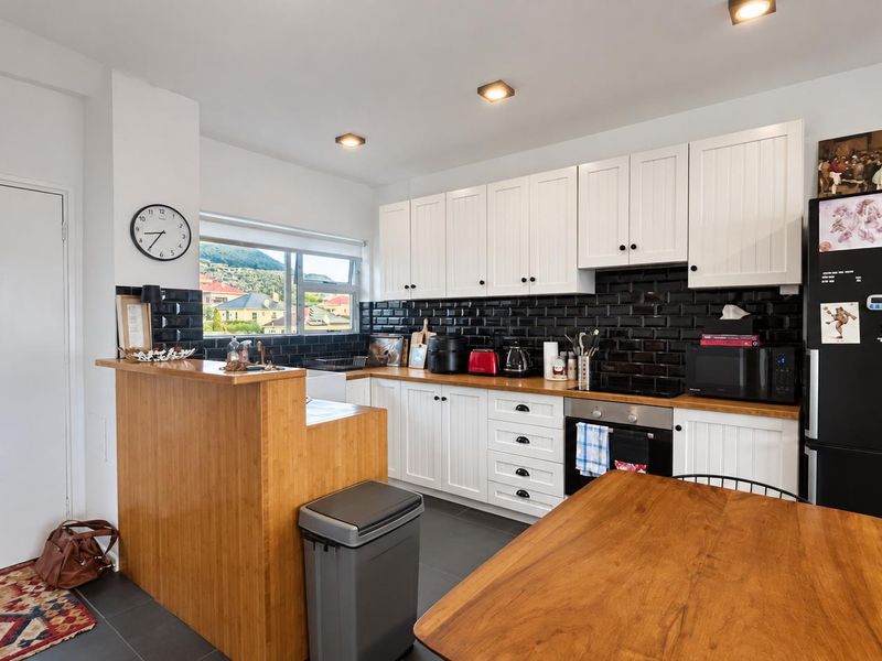 Modern kitchen featuring white shaker cabinetry, black subway tile backsplash, butcher block countertops, and integrated appliances, creating a clean and functional cooking space.