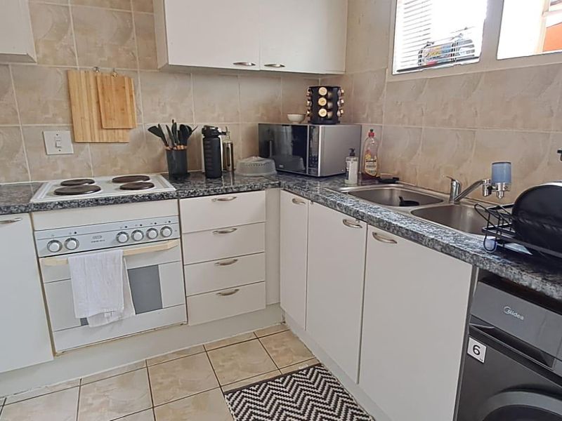 A functional kitchen featuring white cabinetry, granite countertops, a built-in oven with electric hob, and a double sink with tiled backsplash.