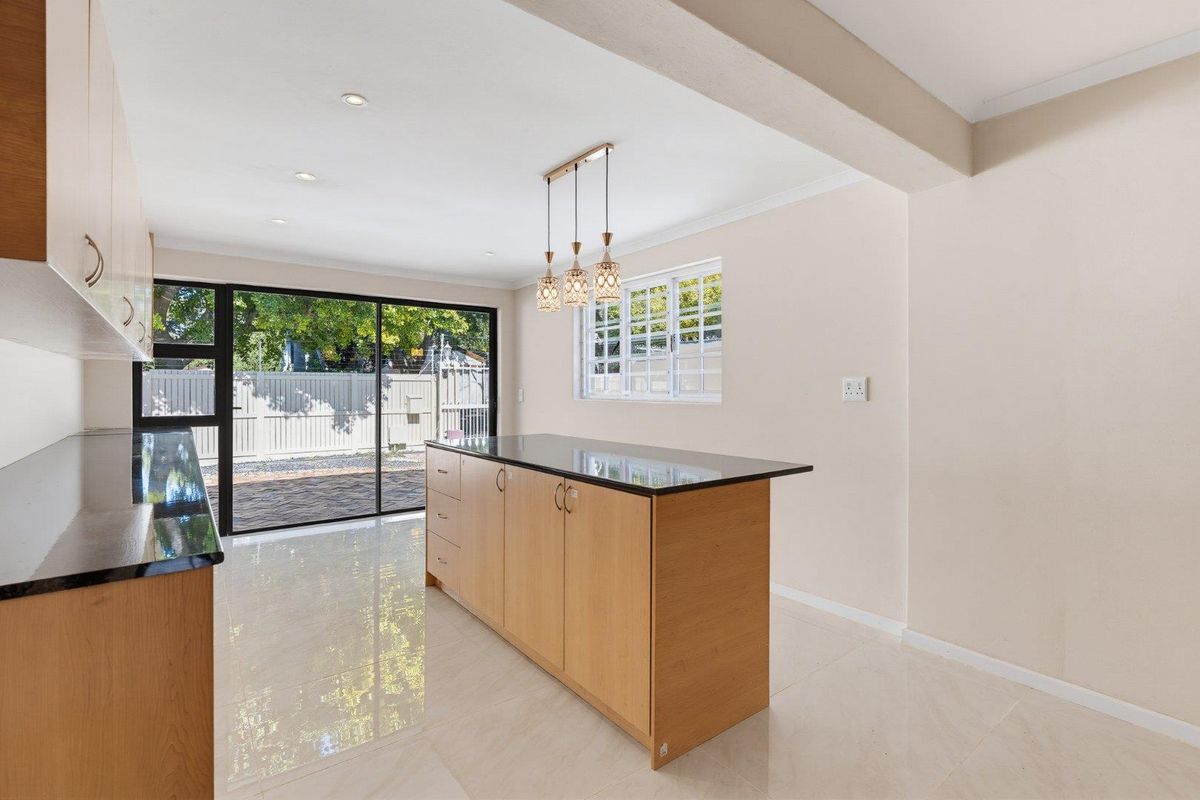 A bright, modern kitchen featuring a central island with granite countertops, light wood cabinetry, tiled flooring, and large sliding doors leading to the exterior.