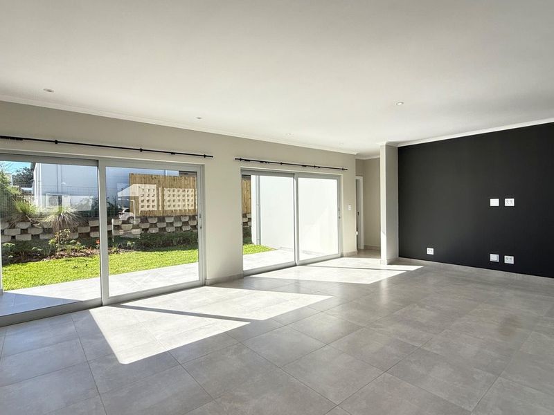 Spacious, light-filled living area featuring large sliding glass doors, neutral tiled flooring, and a modern black accent wall.