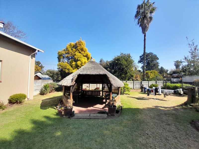 A spacious backyard featuring a traditional thatched gazebo, established lawn, and secure perimeter walling.