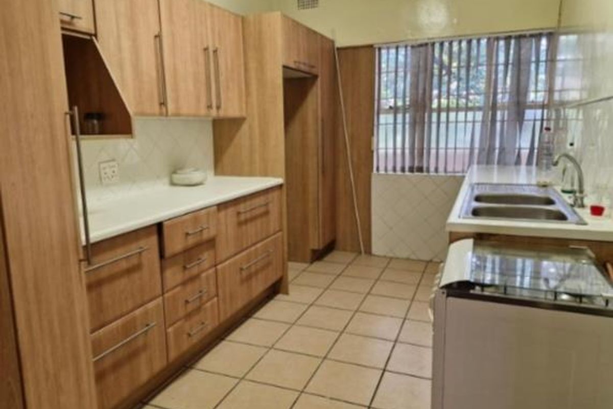 A functional kitchen featuring light wood-tone cabinetry, tiled flooring, and a double stainless steel sink with a window view.