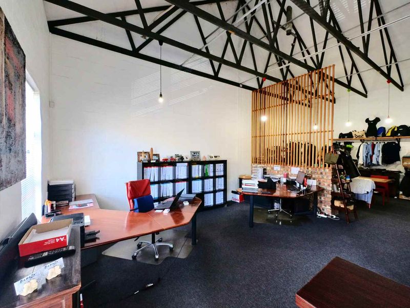 Spacious industrial-style office featuring exposed steel roof trusses, timber slat room dividers, and exposed brick accents, providing a functional and open workspace.